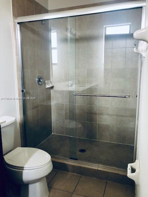 bathroom with a shower with door, tile patterned flooring, and toilet