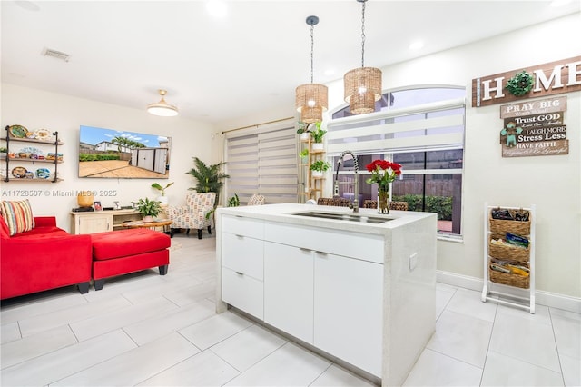 kitchen with light tile patterned flooring, sink, pendant lighting, a kitchen island with sink, and white cabinets