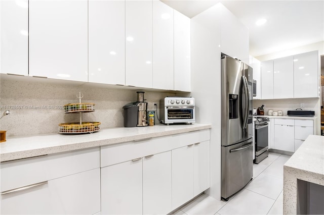 kitchen with white cabinetry, backsplash, stainless steel appliances, light stone counters, and light tile patterned flooring