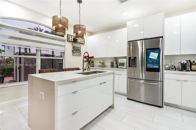 kitchen featuring pendant lighting, an island with sink, sink, white cabinets, and stainless steel fridge