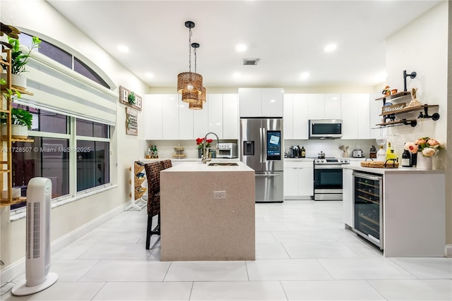 kitchen with appliances with stainless steel finishes, hanging light fixtures, an island with sink, white cabinets, and beverage cooler