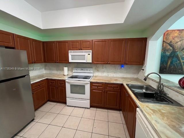 kitchen with tasteful backsplash, sink, light tile patterned floors, and white appliances