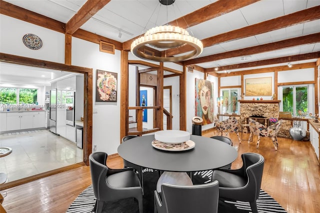 dining room featuring beamed ceiling, a fireplace, and light hardwood / wood-style flooring