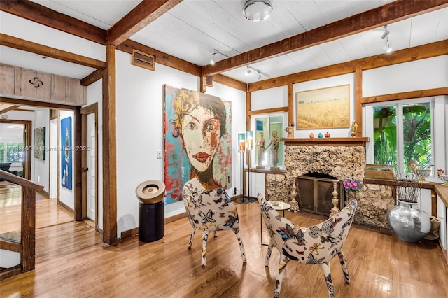 living area featuring beamed ceiling, track lighting, a fireplace, and light wood-type flooring