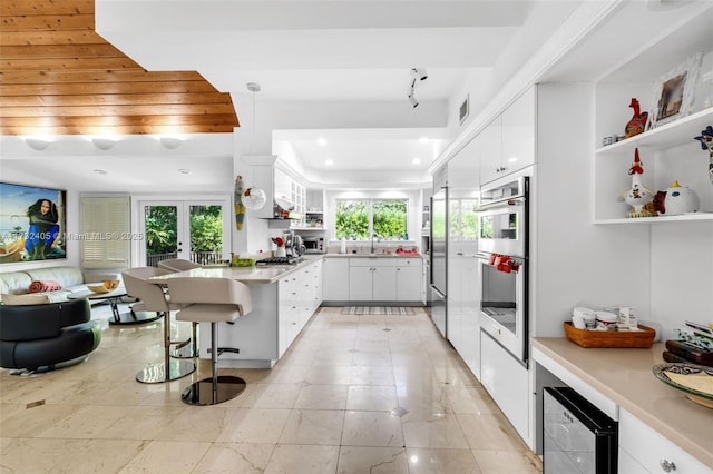 kitchen featuring a kitchen bar, appliances with stainless steel finishes, kitchen peninsula, pendant lighting, and white cabinets