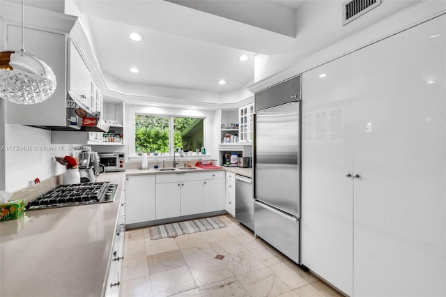 kitchen with pendant lighting, sink, stainless steel appliances, white cabinets, and a raised ceiling