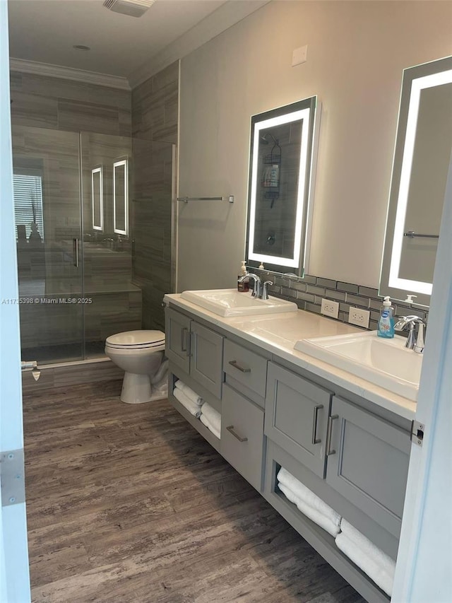 bathroom with toilet, a shower with shower door, crown molding, tasteful backsplash, and wood-type flooring