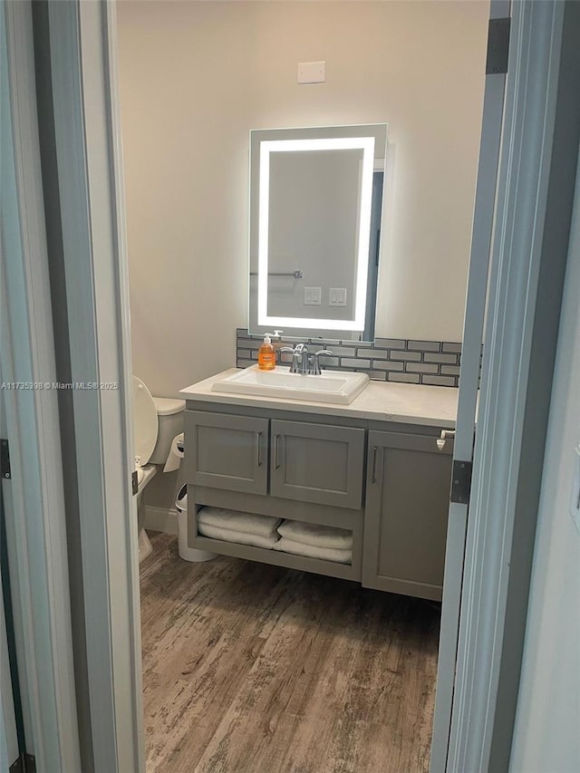 bathroom featuring hardwood / wood-style flooring, vanity, tasteful backsplash, and toilet