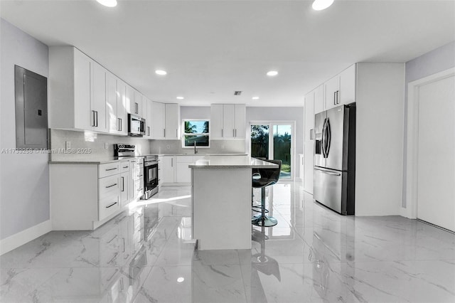 kitchen with white cabinetry, stainless steel appliances, a kitchen breakfast bar, electric panel, and a kitchen island