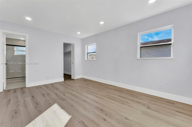 unfurnished bedroom with ensuite bath, a walk in closet, and light hardwood / wood-style floors