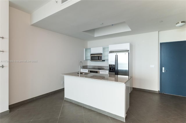 kitchen featuring sink, appliances with stainless steel finishes, white cabinetry, an island with sink, and dark tile patterned flooring