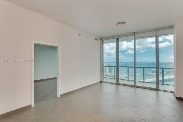 empty room with expansive windows, light tile patterned flooring, and a water view