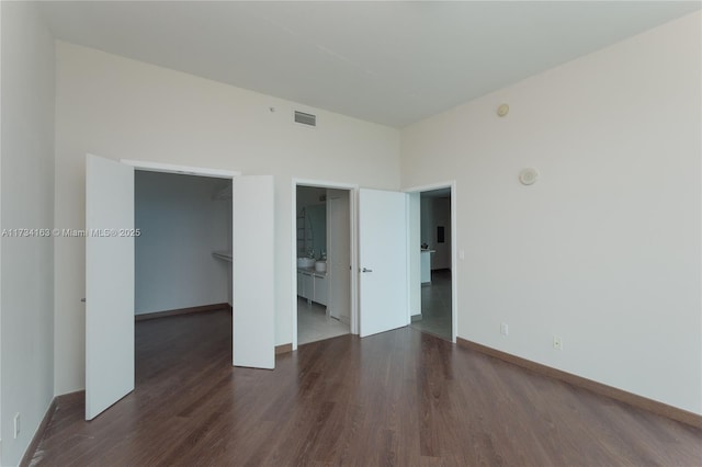 unfurnished bedroom featuring ensuite bathroom, a spacious closet, dark wood-type flooring, and a closet