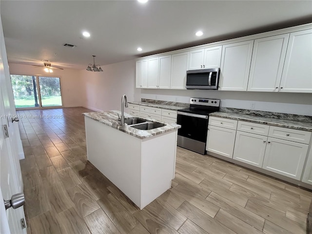 kitchen with visible vents, appliances with stainless steel finishes, white cabinets, a sink, and an island with sink