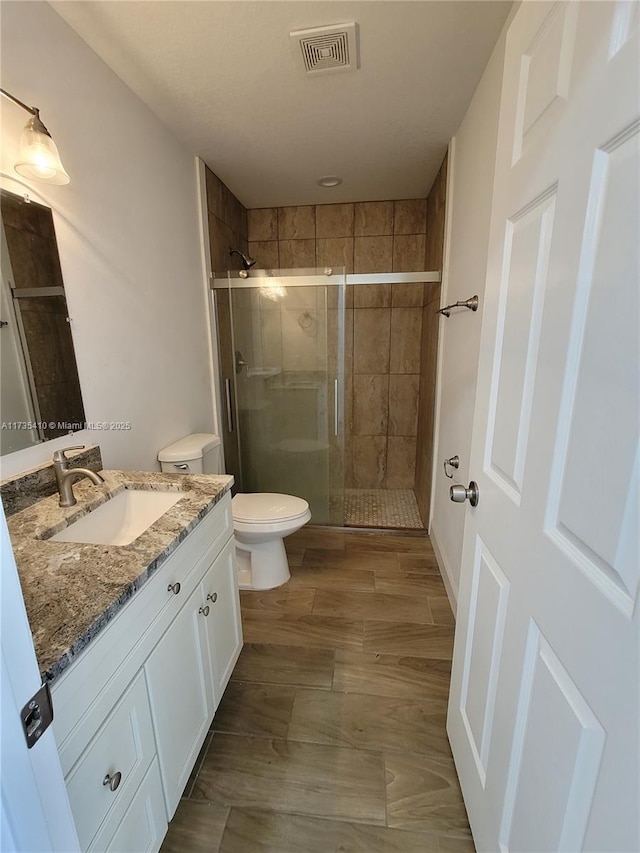 full bathroom with toilet, wood finished floors, vanity, visible vents, and a shower stall