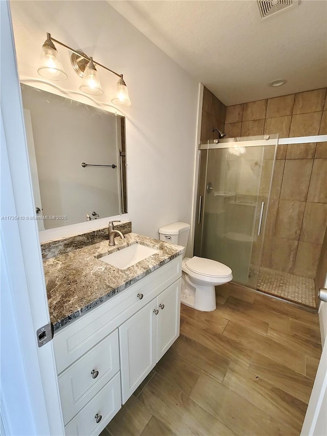 bathroom featuring visible vents, toilet, a shower stall, vanity, and wood finished floors