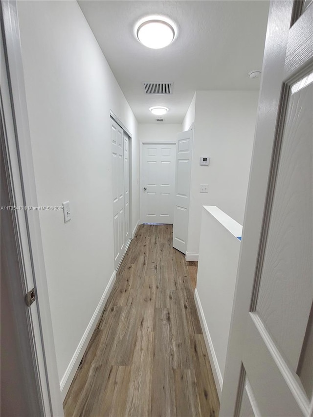 hall with visible vents, an upstairs landing, light wood-style flooring, and baseboards