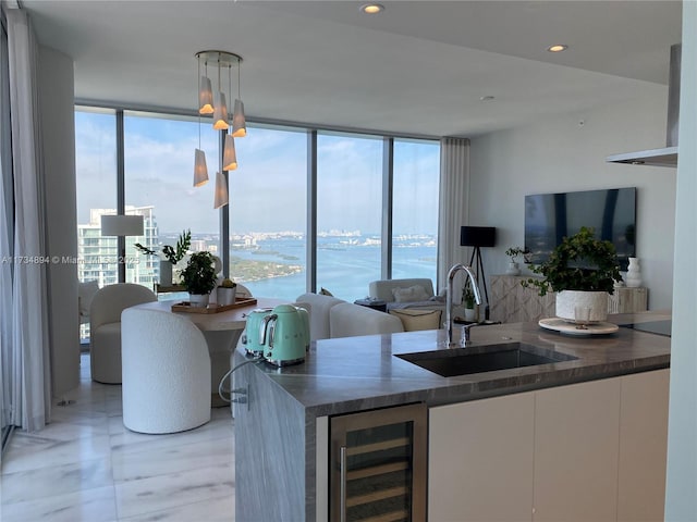 bar with decorative light fixtures, white cabinetry, sink, beverage cooler, and floor to ceiling windows