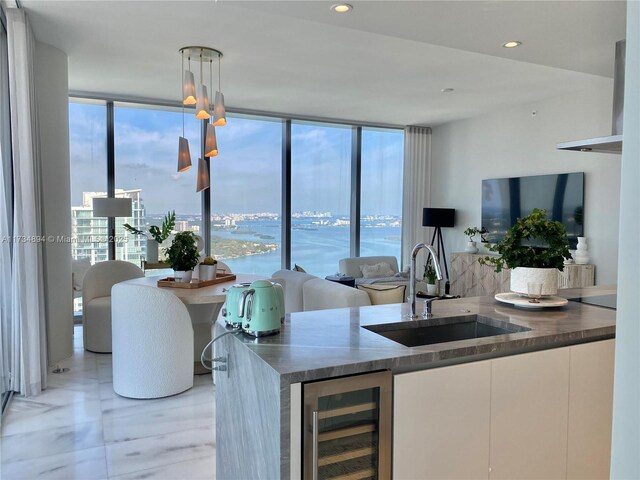 kitchen featuring wine cooler, sink, decorative light fixtures, expansive windows, and white cabinets