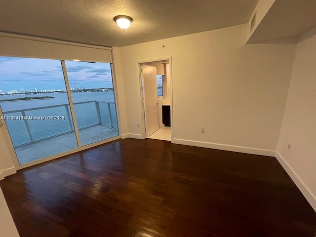 empty room featuring a water view, a textured ceiling, and dark hardwood / wood-style flooring