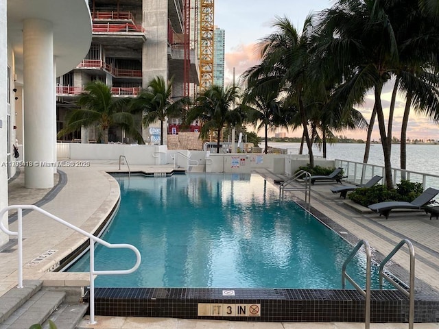 pool at dusk featuring a patio and a water view