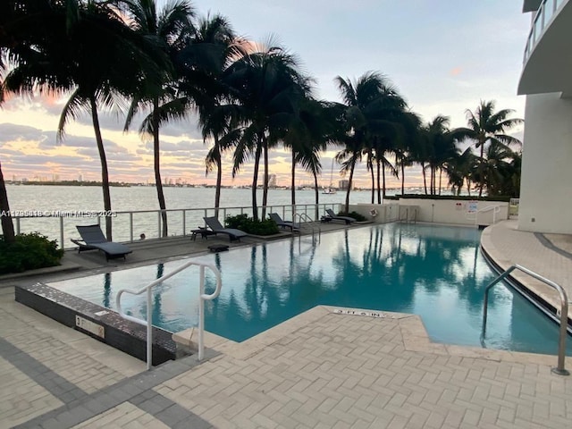 pool at dusk with a water view and a patio area