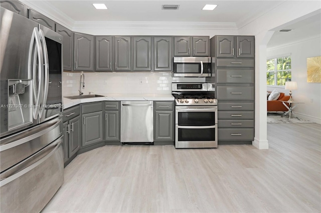 kitchen with sink, appliances with stainless steel finishes, gray cabinetry, ornamental molding, and light wood-type flooring