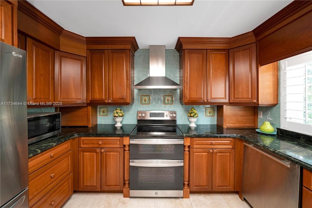 kitchen with dark stone countertops, wall chimney range hood, decorative backsplash, and appliances with stainless steel finishes