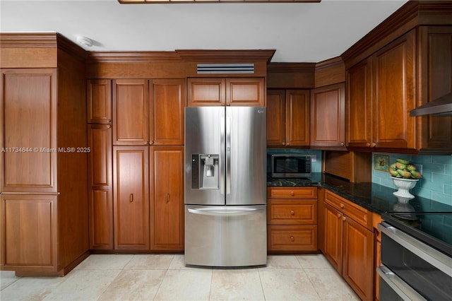 kitchen featuring light tile patterned flooring, tasteful backsplash, dark stone countertops, stainless steel appliances, and wall chimney exhaust hood