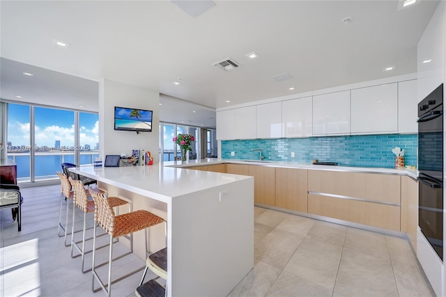 kitchen featuring double oven, backsplash, a kitchen breakfast bar, and white cabinets