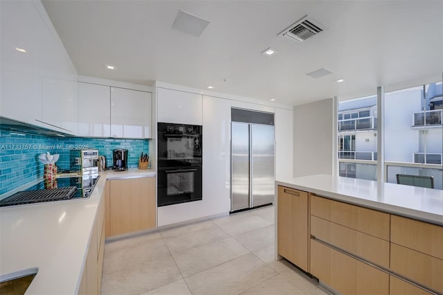 kitchen with backsplash, black double oven, stainless steel built in refrigerator, white cabinets, and light brown cabinetry