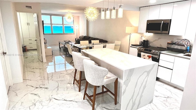 kitchen with white cabinetry, hanging light fixtures, stainless steel appliances, and a kitchen island