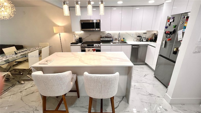 kitchen featuring appliances with stainless steel finishes, decorative light fixtures, white cabinetry, sink, and a breakfast bar area