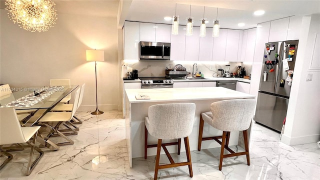 kitchen with appliances with stainless steel finishes, sink, white cabinets, a kitchen bar, and hanging light fixtures