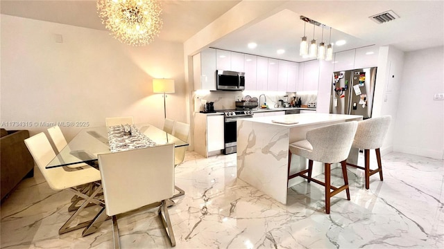 kitchen with a kitchen island, decorative light fixtures, a breakfast bar area, white cabinets, and stainless steel appliances