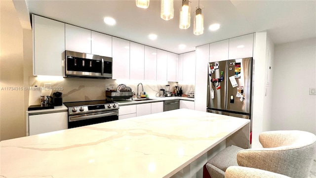 kitchen featuring white cabinetry, sink, a kitchen breakfast bar, hanging light fixtures, and stainless steel appliances