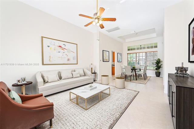 tiled living room featuring a raised ceiling, ceiling fan, and a high ceiling