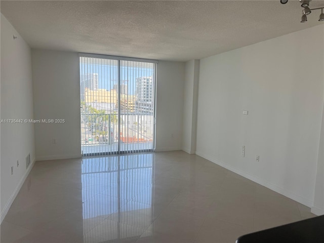 empty room with floor to ceiling windows, a textured ceiling, and light tile patterned floors