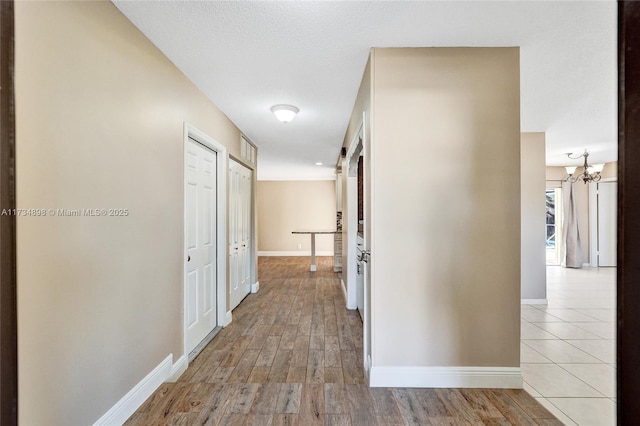 hall featuring an inviting chandelier, light hardwood / wood-style floors, and a textured ceiling