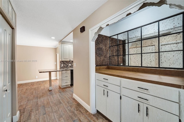 kitchen featuring white cabinetry, light wood-type flooring, backsplash, ornamental molding, and a textured ceiling