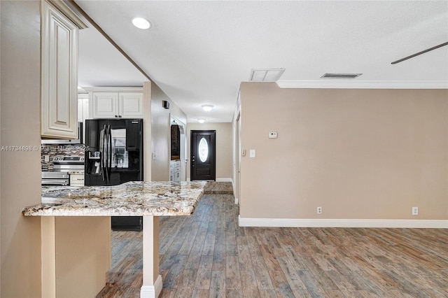 kitchen with a breakfast bar area, hardwood / wood-style floors, light stone countertops, black fridge with ice dispenser, and decorative backsplash