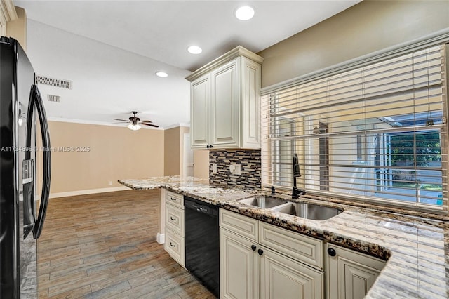 kitchen featuring sink, light stone counters, cream cabinets, decorative backsplash, and black appliances