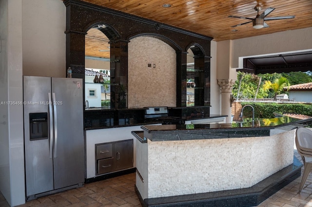 interior space with range, stainless steel fridge with ice dispenser, wooden ceiling, an island with sink, and ceiling fan