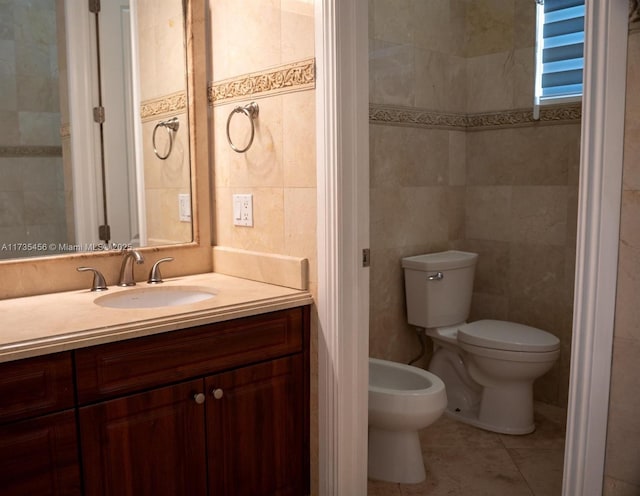 bathroom with a bidet, tile walls, vanity, tile patterned floors, and toilet