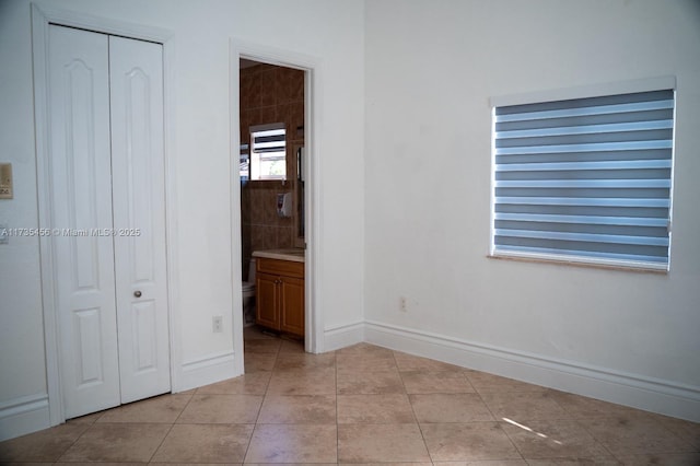 unfurnished bedroom with light tile patterned floors, a closet, and ensuite bathroom