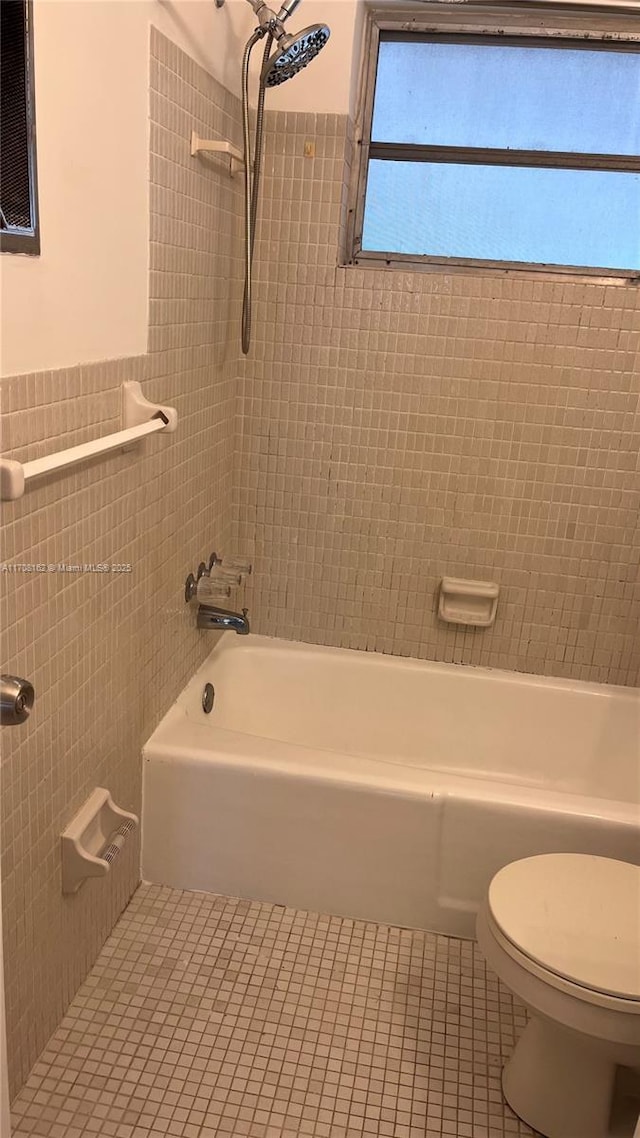 bathroom featuring tile patterned flooring, tiled shower / bath, tile walls, and toilet