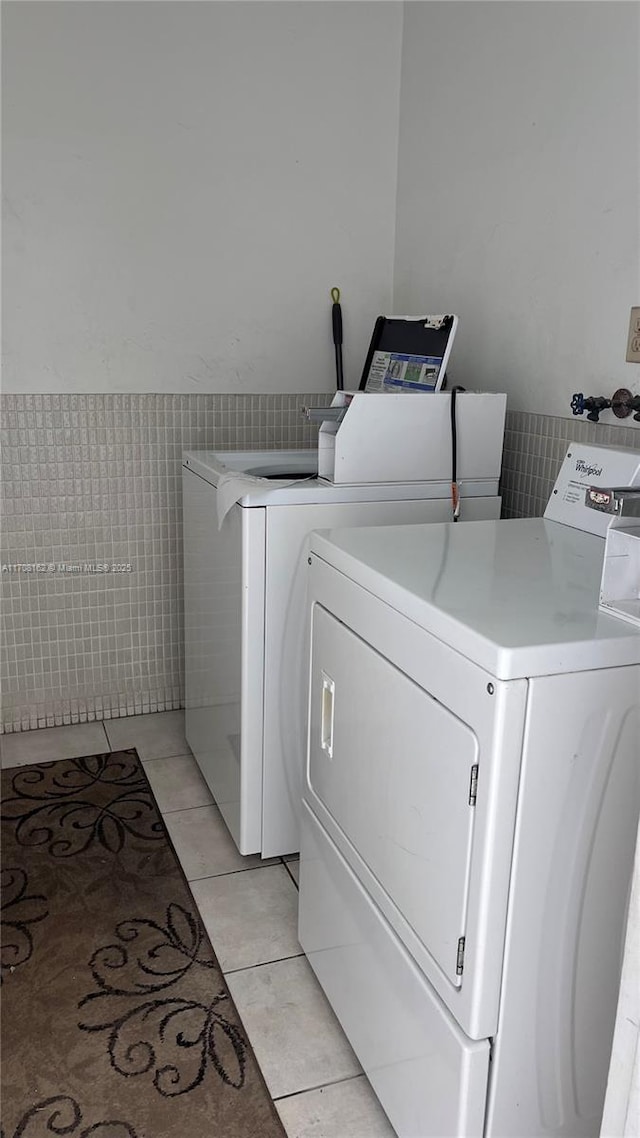 clothes washing area with tile walls, washing machine and dryer, and light tile patterned flooring