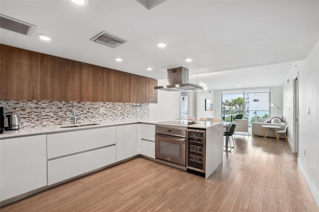 kitchen with sink, white cabinetry, kitchen peninsula, island exhaust hood, and oven