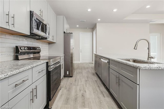 kitchen featuring stainless steel appliances, gray cabinets, light stone countertops, and sink