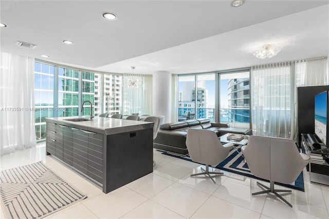 kitchen featuring expansive windows, light tile patterned flooring, sink, and a center island with sink